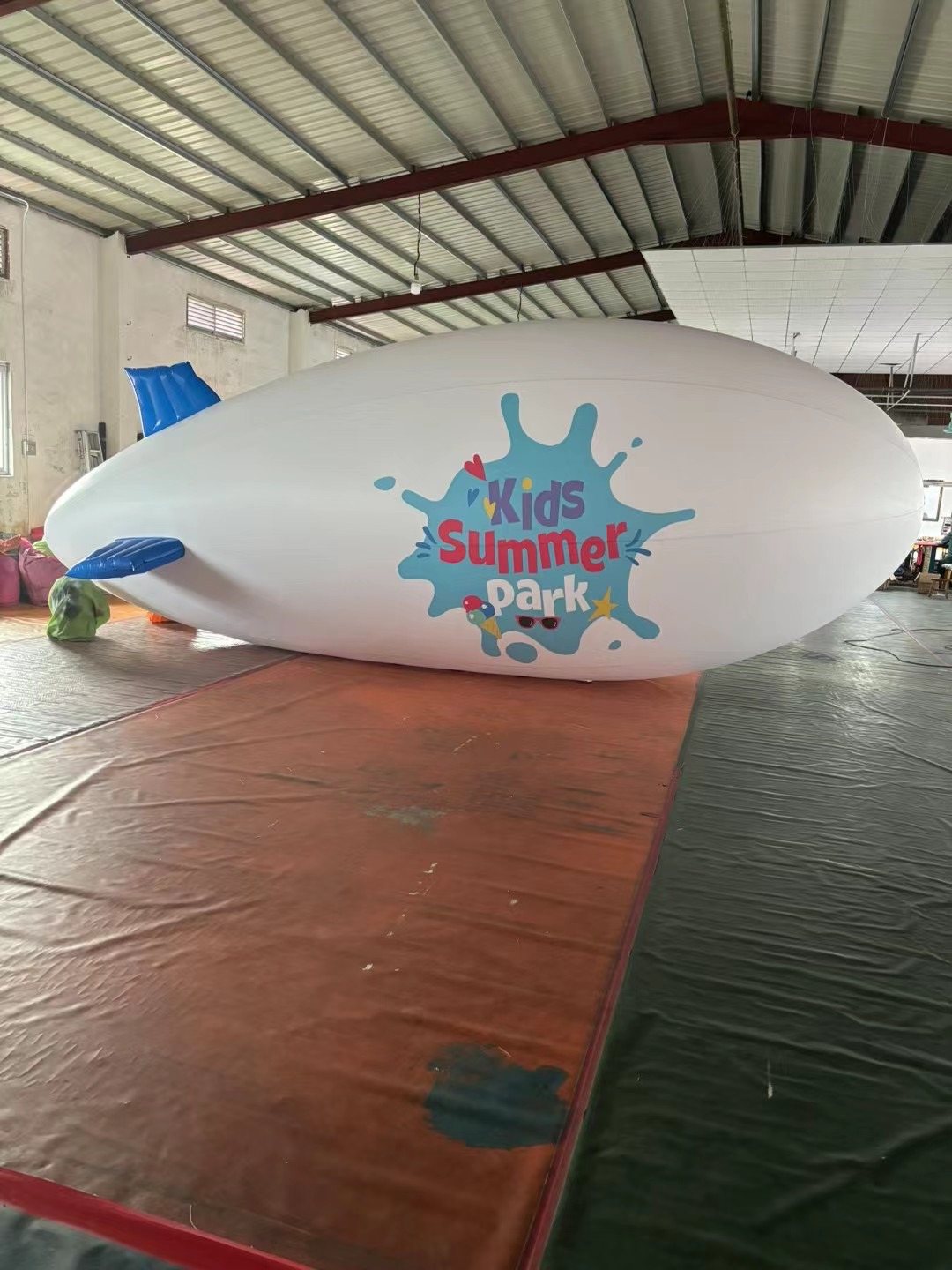 White custom advertising blimp fully inflated on a factory floor for testing.