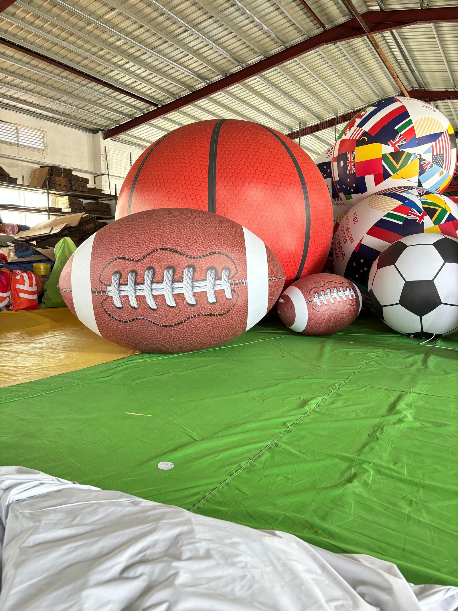 Oversized basketball, football, rugby ball, and soccer ball inflatables on a factory floor for testing.